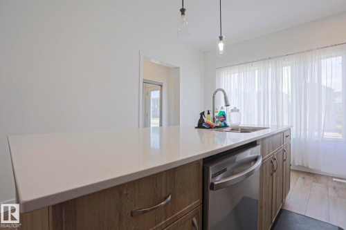 Kitchen island featuring a white countertop, wood-finish cabinetry, and stainless steel dishwasher - 33 Eton Link, Spruce Grove, AB 