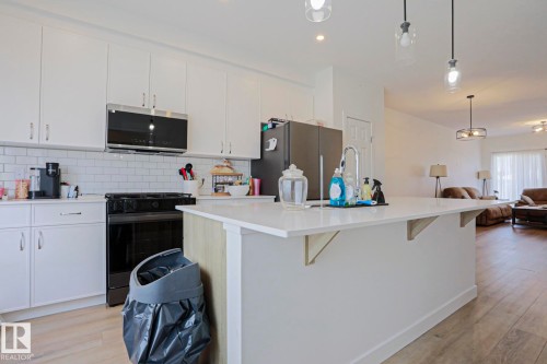 Modern kitchen featuring white cabinetry, subway tile backsplash, and stainless steel microwave - 33 Eton Link, Spruce Grove, AB 