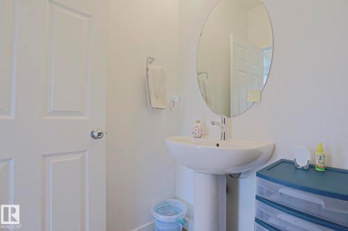 Pedestal sink with a polished chrome faucet, oval frameless mirror, and a panel interior door - 33 Eton Link, Spruce Grove, AB 