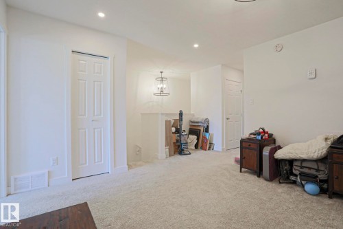 Carpeted interior area featuring white walls, recessed ceiling lighting, and a prominent chandelier with an open-cage design - 33 Eton Link, Spruce Grove, AB 