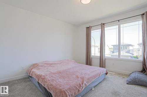 Bright room featuring a large window with white trim, light gray carpeting, neutral wall paint, and a flush-mount ceiling light - 33 Eton Link, Spruce Grove, AB 