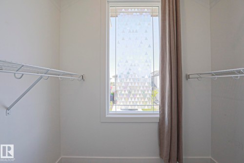 Closet space featuring white wire shelving, a window with patterned privacy film, and a neutral-toned curtain - 33 Eton Link, Spruce Grove, AB 
