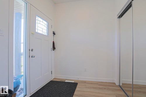 Entryway featuring a white paneled door with decorative glass inserts, a full-length sidelight, wood-finish flooring, and a mirrored sliding closet door - 33 Eton Link, Spruce Grove, AB 