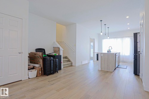 Open-concept living area featuring wood-finish flooring, a kitchen island with integrated sink, pendant lighting, and recessed ceiling lights - 33 Eton Link, Spruce Grove, AB 