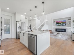 Open-concept living area featuring a kitchen island with pendant lighting, stainless steel appliances, wood-finish flooring, a white stone fireplace surround, and built-in shelving - 