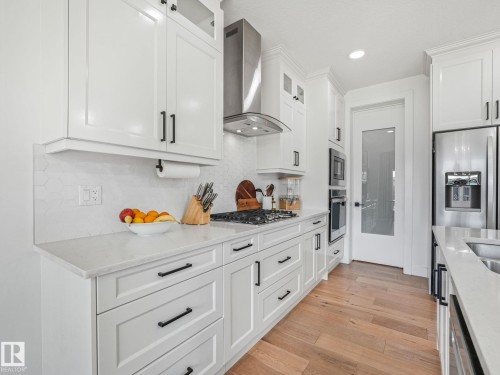 Contemporary kitchen featuring white cabinetry, light-toned countertops, stainless steel appliances, a tile backsplash, and wood-finish flooring - 5411 66 Street, Beaumont, AB 