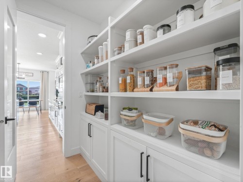 Bright walk-in pantry featuring extensive built-in shelving, lower cabinetry with black hardware, and wood-finish flooring extending into an adjacent living space - 5411 66 Street, Beaumont, AB 