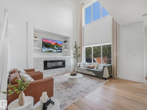 Two-story living area featuring a stone-clad fireplace with built-in media center, expansive windows, wood-finish flooring, and high ceilings - 5411 66 Street, Beaumont, AB 