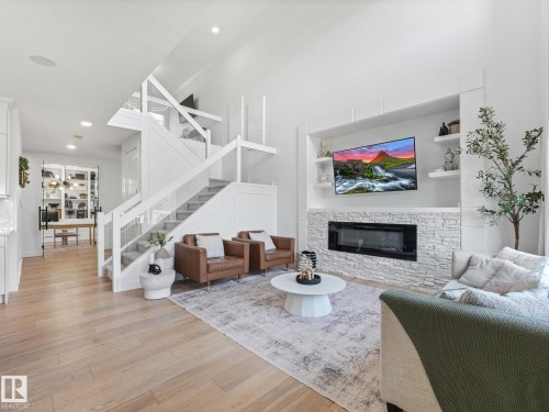 Open-concept living area featuring high ceilings, light wood-finish flooring, and a modern fireplace with white stacked stone surround - 5411 66 Street, Beaumont, AB 