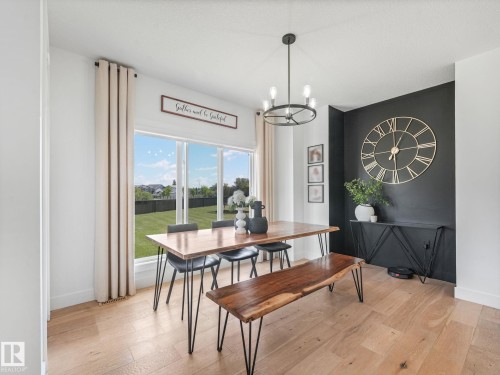 Dining area featuring wood-finish flooring, a large window overlooking the yard, and a black accent wall - 5411 66 Street, Beaumont, AB 