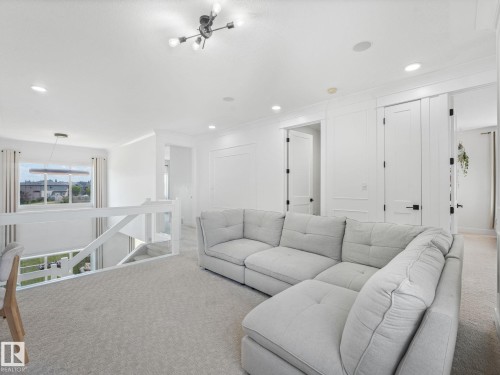 Carpeted upper-level landing featuring a contemporary chandelier, recessed lighting, white paneled doors with black hardware, and an open railing overlooking the lower level - 5411 66 Street, Beaumont, AB 