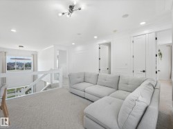 Carpeted upper-level landing featuring a contemporary chandelier, recessed lighting, white paneled doors with black hardware, and an open railing overlooking the lower level - 