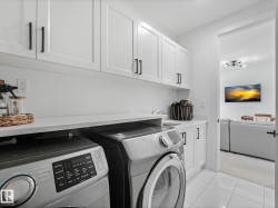 Laundry area featuring white shaker-style cabinetry, matte black hardware, and a light-toned countertop - 