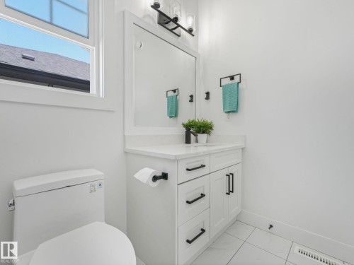 White vanity with a rectangular undermount sink, a countertop with a light marble-style finish, and matte black hardware - 5411 66 Street, Beaumont, AB 