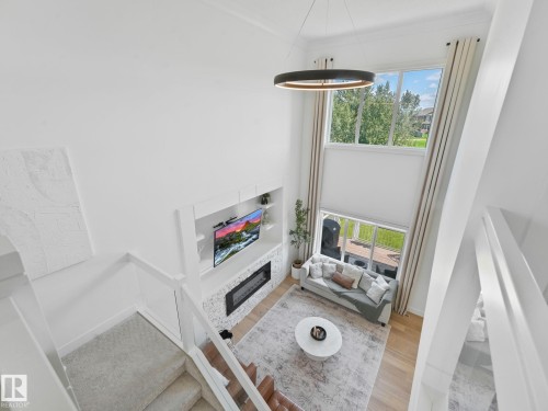 Two-story living area featuring tall windows with exterior views, a built-in entertainment center, a fireplace with stone surround, and light wood-finish flooring - 5411 66 Street, Beaumont, AB 