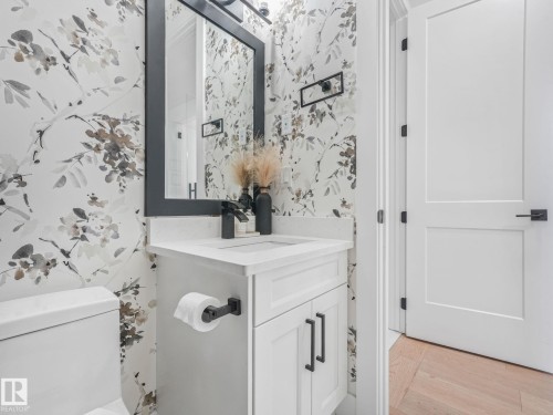 Powder room featuring a single vanity with a white cabinet, integrated sink, and matte black faucet - 5411 66 Street, Beaumont, AB 