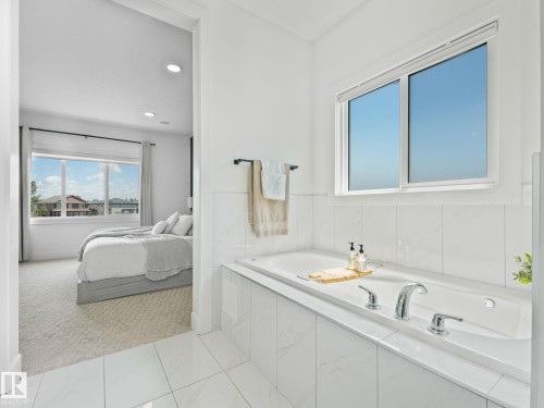 Soaking tub with chrome fixtures and white subway tile surround, illuminated by natural light from a large window - 5411 66 Street, Beaumont, AB 