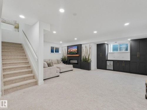 Spacious lower-level living area featuring recessed lighting, plush carpet flooring, a built-in media center with an electric fireplace, and extensive dark-toned cabinetry with a beverage refrigerator - 5411 66 Street, Beaumont, AB 