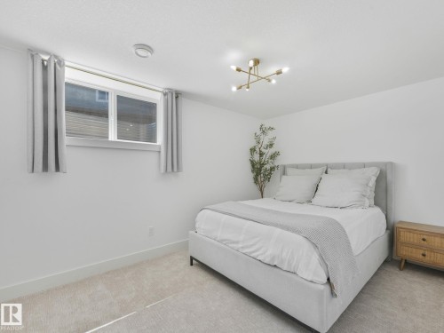 Bedroom featuring light-toned carpeting, a window with white trim, and a gold-tone sputnik light fixture - 5411 66 Street, Beaumont, AB 