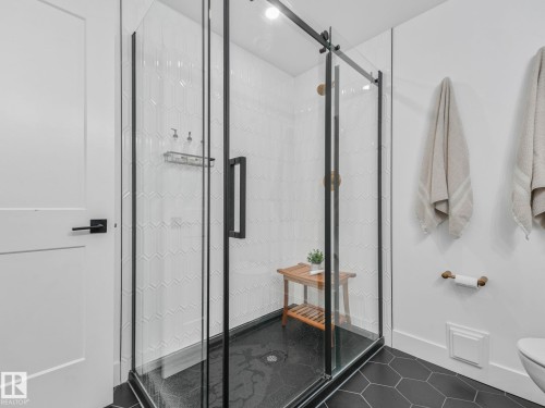 Frameless glass shower enclosure with matte black hardware, white chevron-patterned tile, a black hexagonal tile floor, and a matte black shower system - 5411 66 Street, Beaumont, AB 