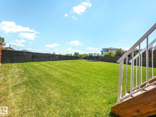 Expansive backyard featuring a manicured lawn, full perimeter fencing, and a sturdy exterior staircase with white railings - 5411 66 Street, Beaumont, AB 