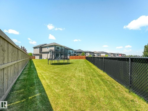Spacious backyard featuring a manicured lawn, wood privacy fence, and black chain-link fencing - 5411 66 Street, Beaumont, AB 