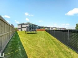 Spacious backyard featuring a manicured lawn, wood privacy fence, and black chain-link fencing - 