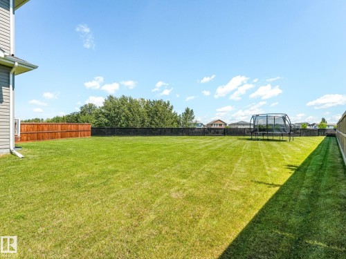 Expansive backyard featuring a manicured lawn, full perimeter fencing, and mature tree line - 5411 66 Street, Beaumont, AB 
