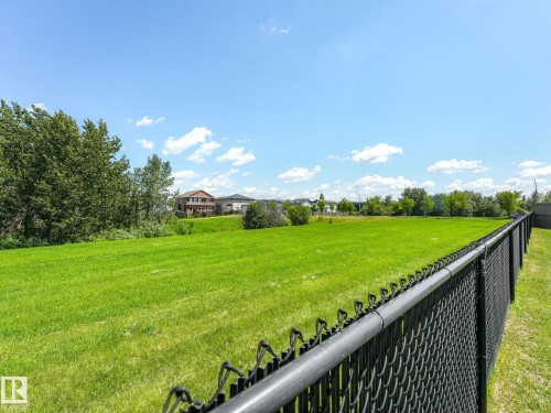 Expansive green space featuring a chain-link fence, surrounding trees, and distant residential structures - 5411 66 Street, Beaumont, AB 