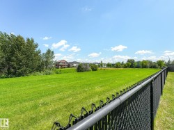 Expansive green space featuring a chain-link fence, surrounding trees, and distant residential structures - 