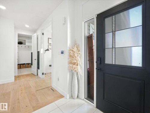 Entryway featuring a black front door with decorative glass inserts, wood-finish flooring, white tile flooring, and clean white walls - 5411 66 Street, Beaumont, AB 