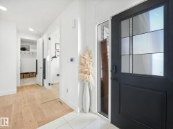 Entryway featuring a black front door with decorative glass inserts, wood-finish flooring, white tile flooring, and clean white walls - 