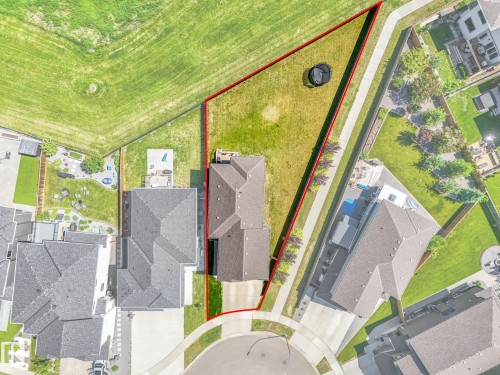 Expansive property outlined by a red boundary, featuring a large grassy lot, a multi-gabled roofline, a concrete driveway, and established landscaping - 5411 66 Street, Beaumont, AB 