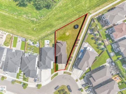 Aerial view of a residential property with a sloped, grassy backyard bordered by a paved pathway and a large open green space - 5411 66 Street, Beaumont, AB 