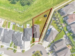 Aerial view of a residential property with a sloped, grassy backyard bordered by a paved pathway and a large open green space - 