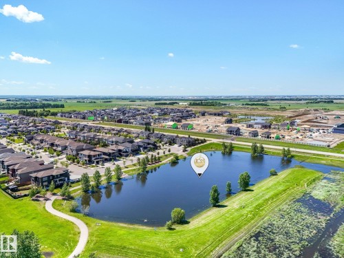 Aerial perspective of a developed residential community featuring a prominent central lake, surrounding green spaces, and paved walking paths - 5411 66 Street, Beaumont, AB 