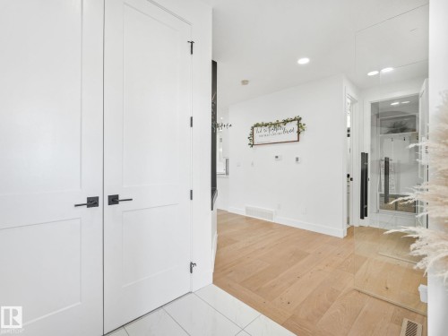 Entryway featuring white panel doors with matte black hardware, tile flooring, and light wood-finish flooring extending into the interior - 5411 66 Street, Beaumont, AB 