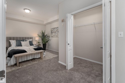 Carpeted bedroom featuring a gray upholstered headboard, a ceiling-mounted light fixture, and a spacious closet with bi-fold doors and wire shelving - 404 12111 51 Avenue, Edmonton, AB 