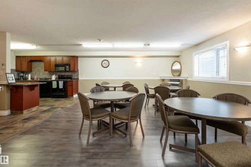 Spacious common area featuring wood-finish flooring, a full kitchen with dark cabinetry and black appliances, and ample natural light from the window - 404 12111 51 Avenue, Edmonton, AB 