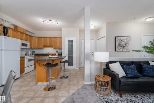 Open-concept kitchen featuring wood cabinetry, white appliances, and a central island with bar seating - 404 12111 51 Avenue, Edmonton, AB 
