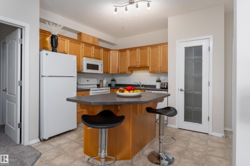 Kitchen featuring light wood cabinetry and a peninsula with a dark countertop - 404 12111 51 Avenue, Edmonton, AB 