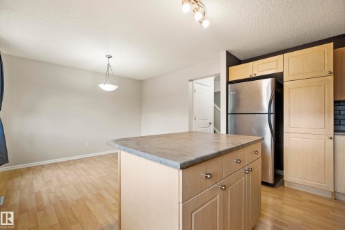 Kitchen island featuring a solid surface countertop and built-in cabinetry, stainless steel refrigerator, wood-finish flooring, and a dining area with a suspended light fixture - 2369 27 Avenue, Edmonton, AB 