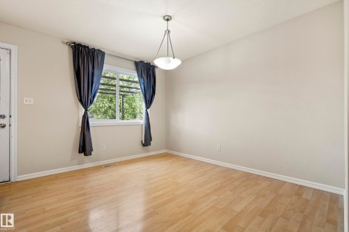 Bright interior space featuring light-toned wood-finish flooring, a white trim baseboard, and a neutral wall color - 2369 27 Avenue, Edmonton, AB 