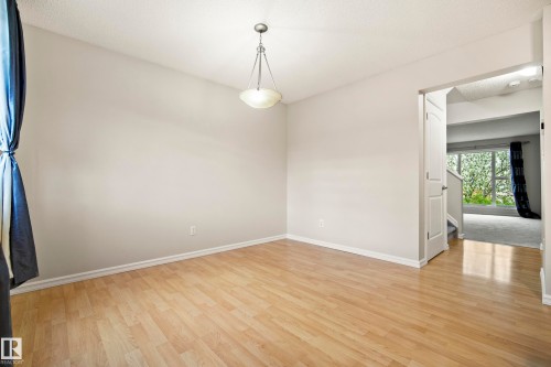 Spacious room with wood-finish flooring, light neutral wall tones, and a suspended ceiling fixture - 2369 27 Avenue, Edmonton, AB 