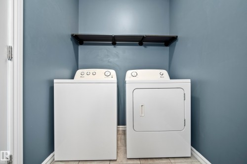 Laundry area featuring a top-load washing machine, front-load dryer, and a wall-mounted shelving unit - 2369 27 Avenue, Edmonton, AB 