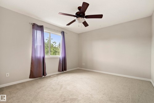 Bedroom featuring light gray walls, plush carpet, a ceiling fan with integrated lighting, and a window with a tree-lined backdrop - 2369 27 Avenue, Edmonton, AB 