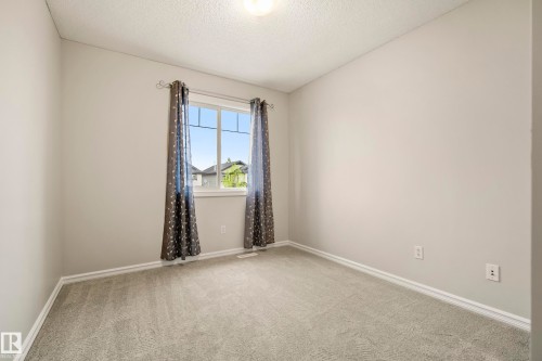 Neutral-toned room featuring a window with patterned drapes, light gray carpeting, and white baseboards - 2369 27 Avenue, Edmonton, AB 