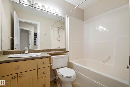 Bathroom featuring a single vanity with wood-finish cabinetry, an integrated sink, and a large mirror with overhead vanity lighting - 2369 27 Avenue, Edmonton, AB 