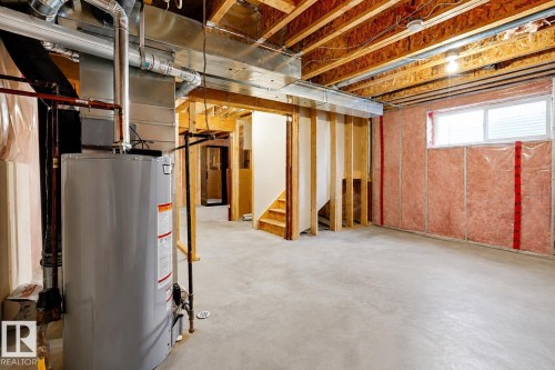 Unfinished basement featuring a concrete floor, exposed wood joists, and a hot water heater - 2369 27 Avenue, Edmonton, AB 