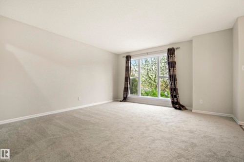 Spacious interior room featuring light gray carpeting, neutral wall paint, white baseboards, and a large window with white trim - 2369 27 Avenue, Edmonton, AB 